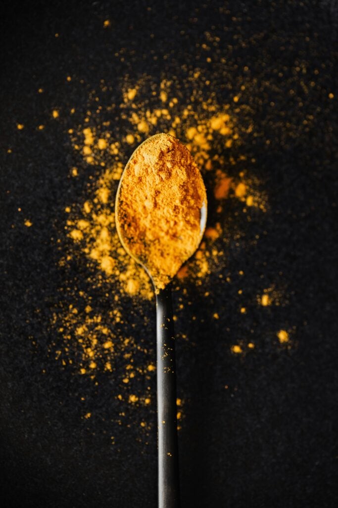 Image d'une cuillère contenant des épices orangées, symbolisant l'utilisation du curcuma dans nos rituels de beauté naturelle, sur fond noir