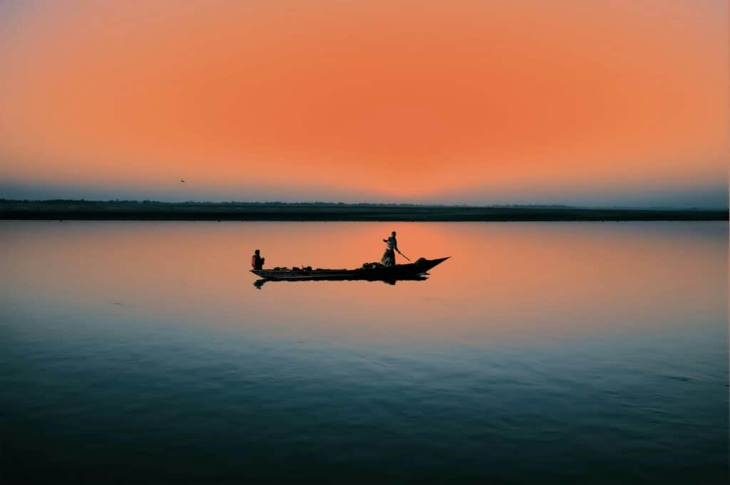 Deux personnes sur une pirogue au milieu d'un fleuve bleu et orangé