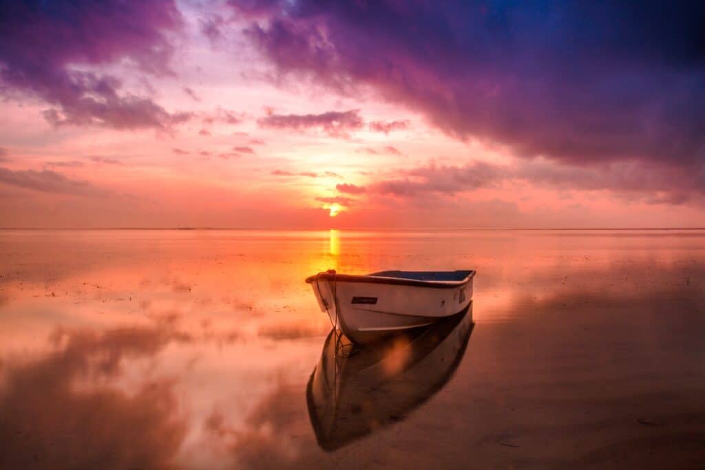 Image d'une barque sur une plage à marée basse, avec une mer calme en arrière-plan et un coucher de soleil rose et orange