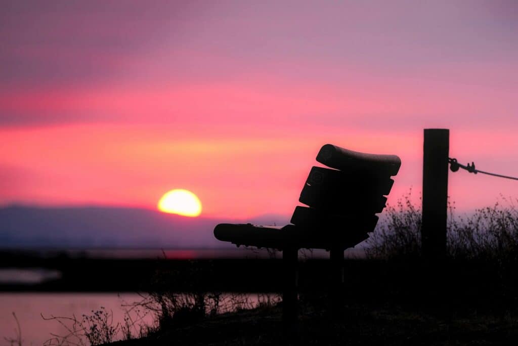 Aide de la naturopathie dans le deuil : ciel rose et violet avec un banc vide et un coucher de soleil au loin