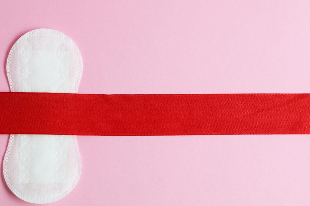 Serviette menstruelle blanche et rouge sur fond rose, évoquant soin et confort pendant les règles douloureuses