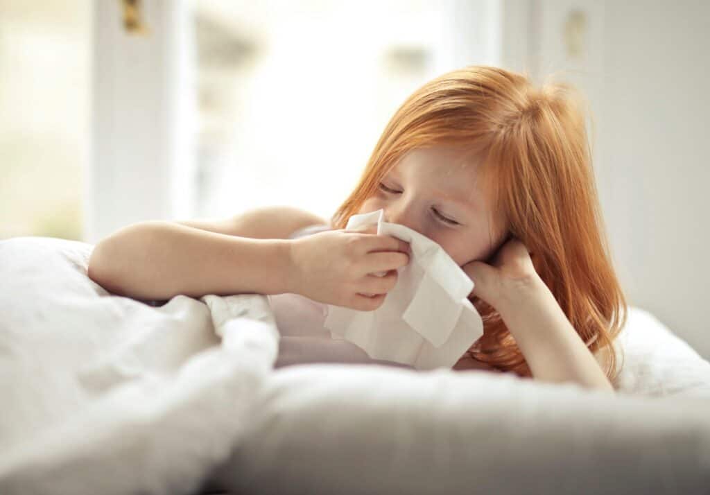 Enfant enrhumé allongé dans son lit, se mouchant à cause d’un rhume hivernal